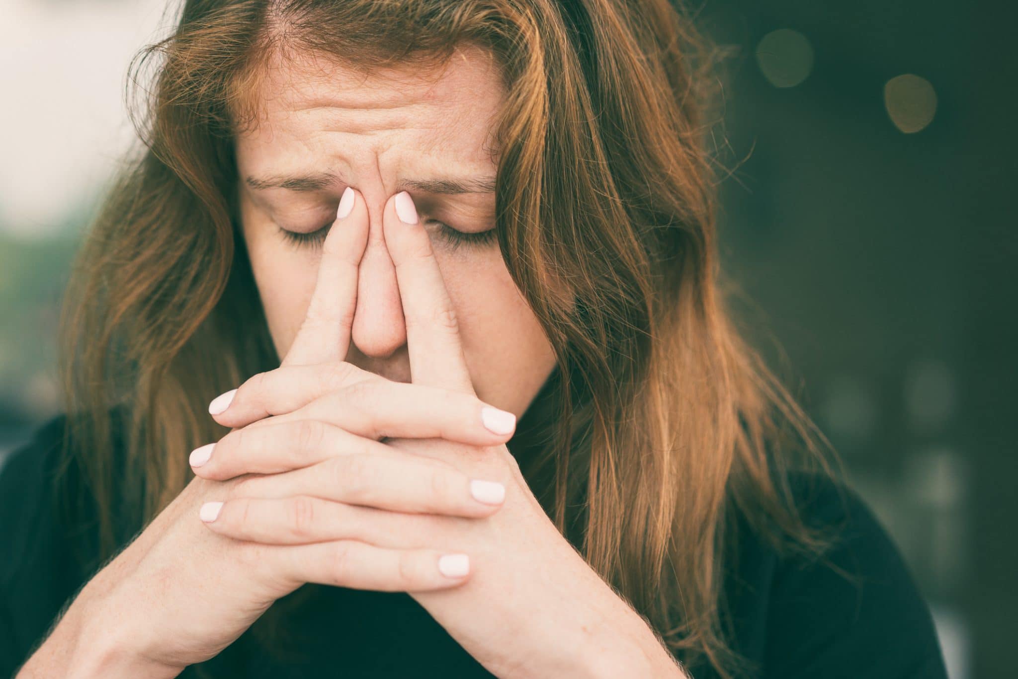 Closeup of young woman with closed eyes massaging her nose bridge with fingers.