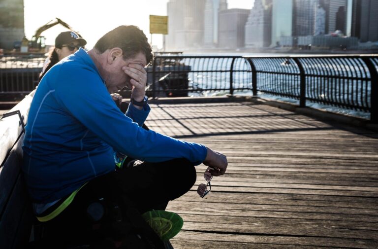 Man sitting on a bench on a pier rubbing his eyes out of exhaustion