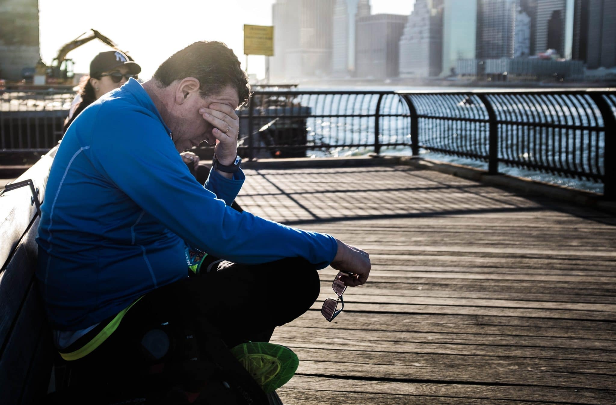 Man sitting on a bench on a pier rubbing his eyes out of exhaustion