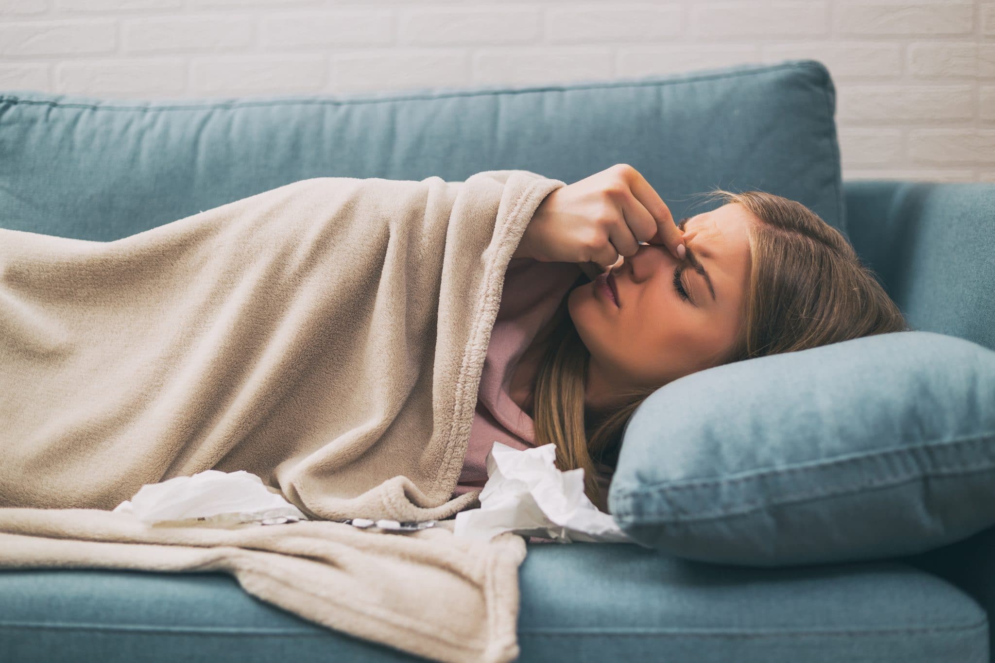 Woman lying down on a couch pinching the bridge of her nose