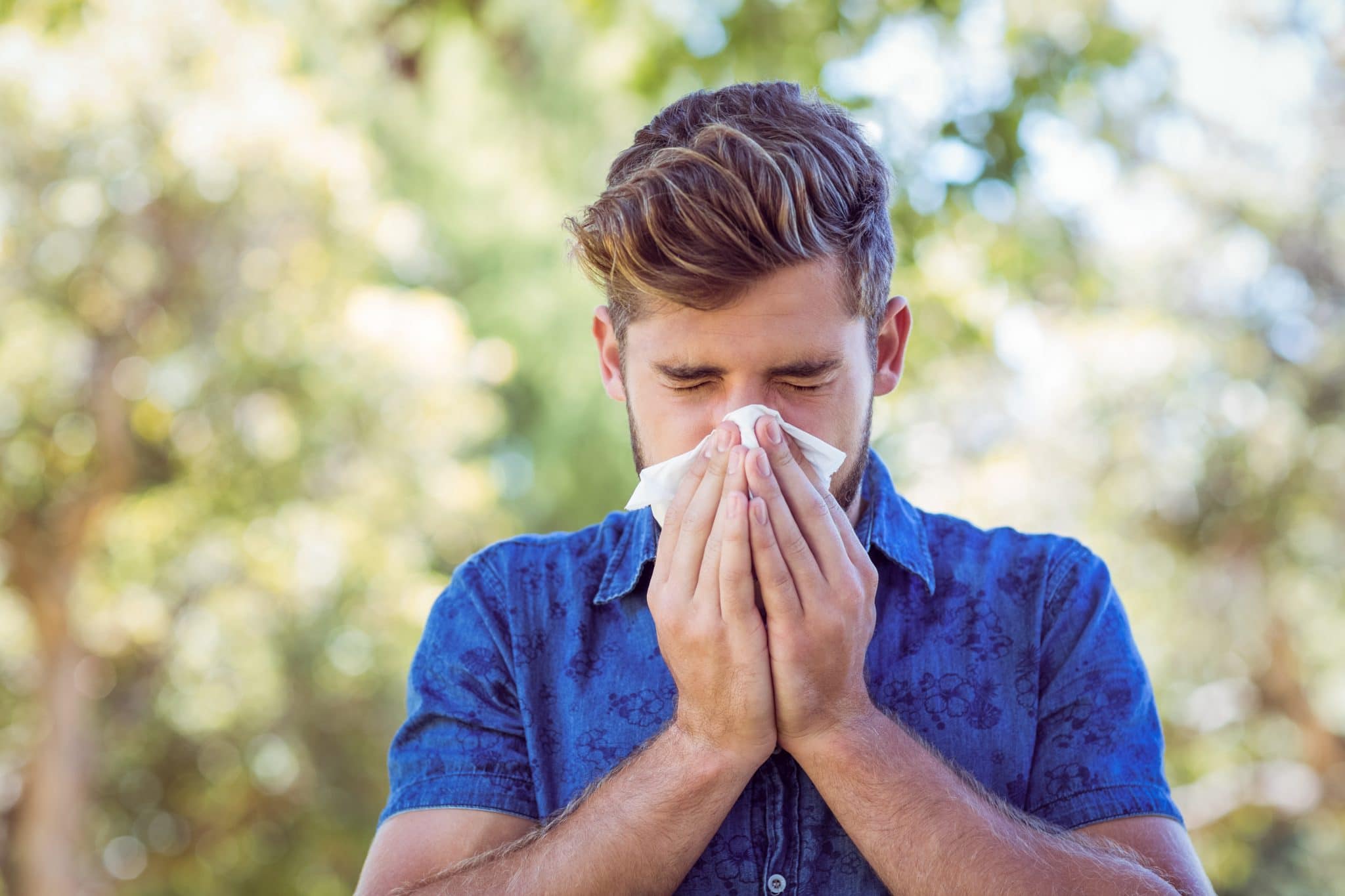 Man blowing his nose while outside in a park.