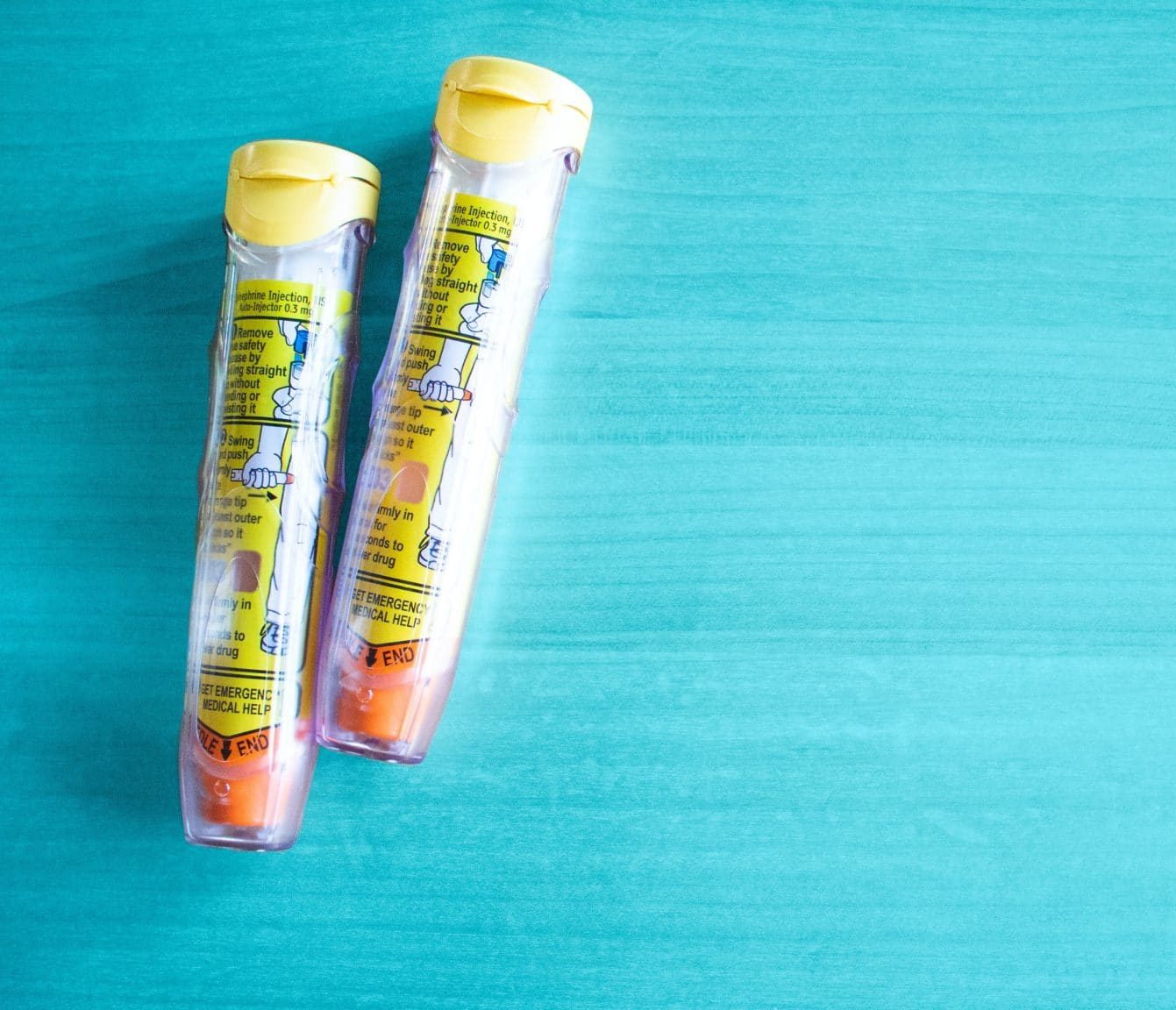 Picture of two EpiPens behind a teal background.