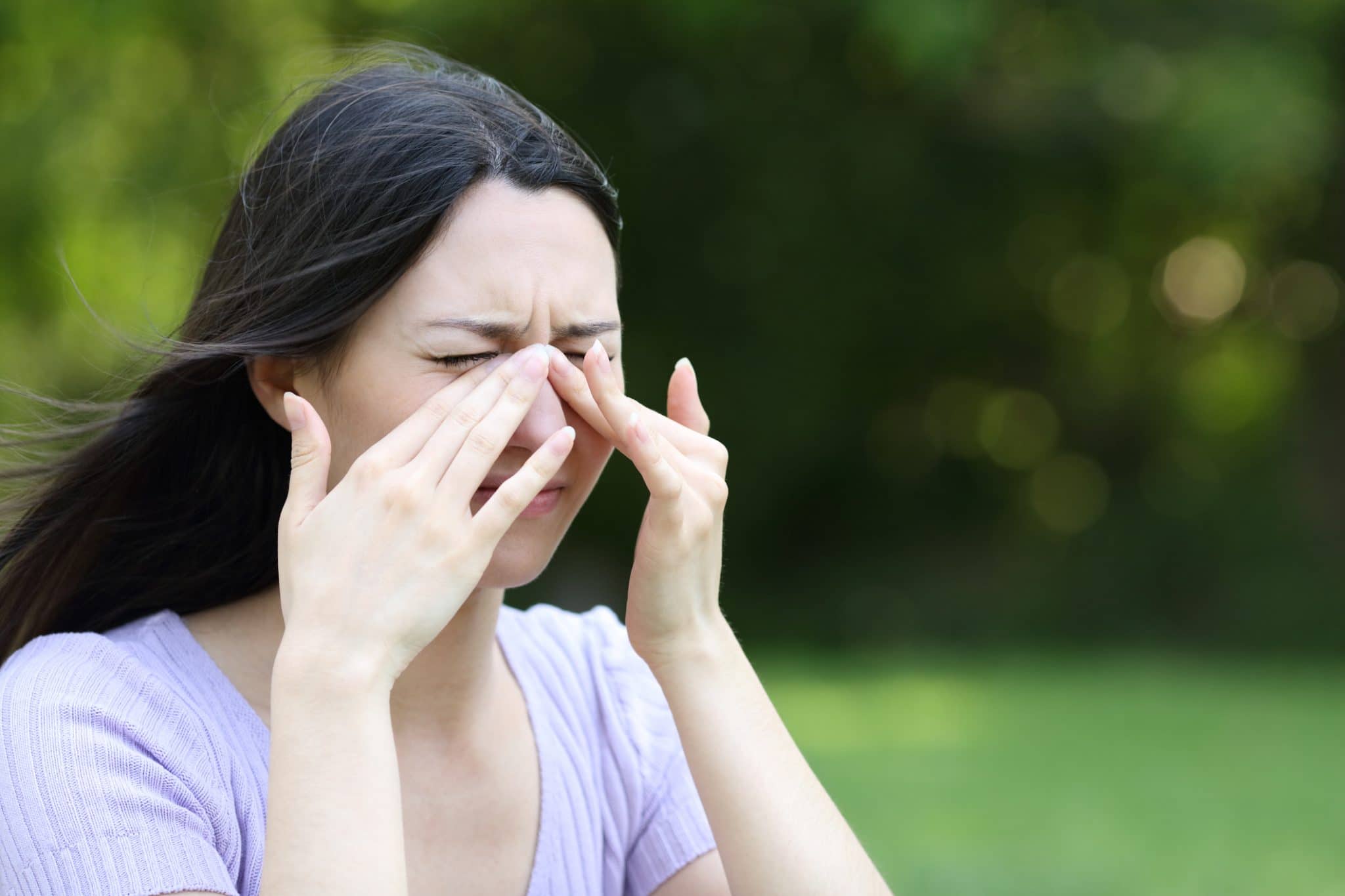 Woman experiencing sinus pressure in an outdoor environment.