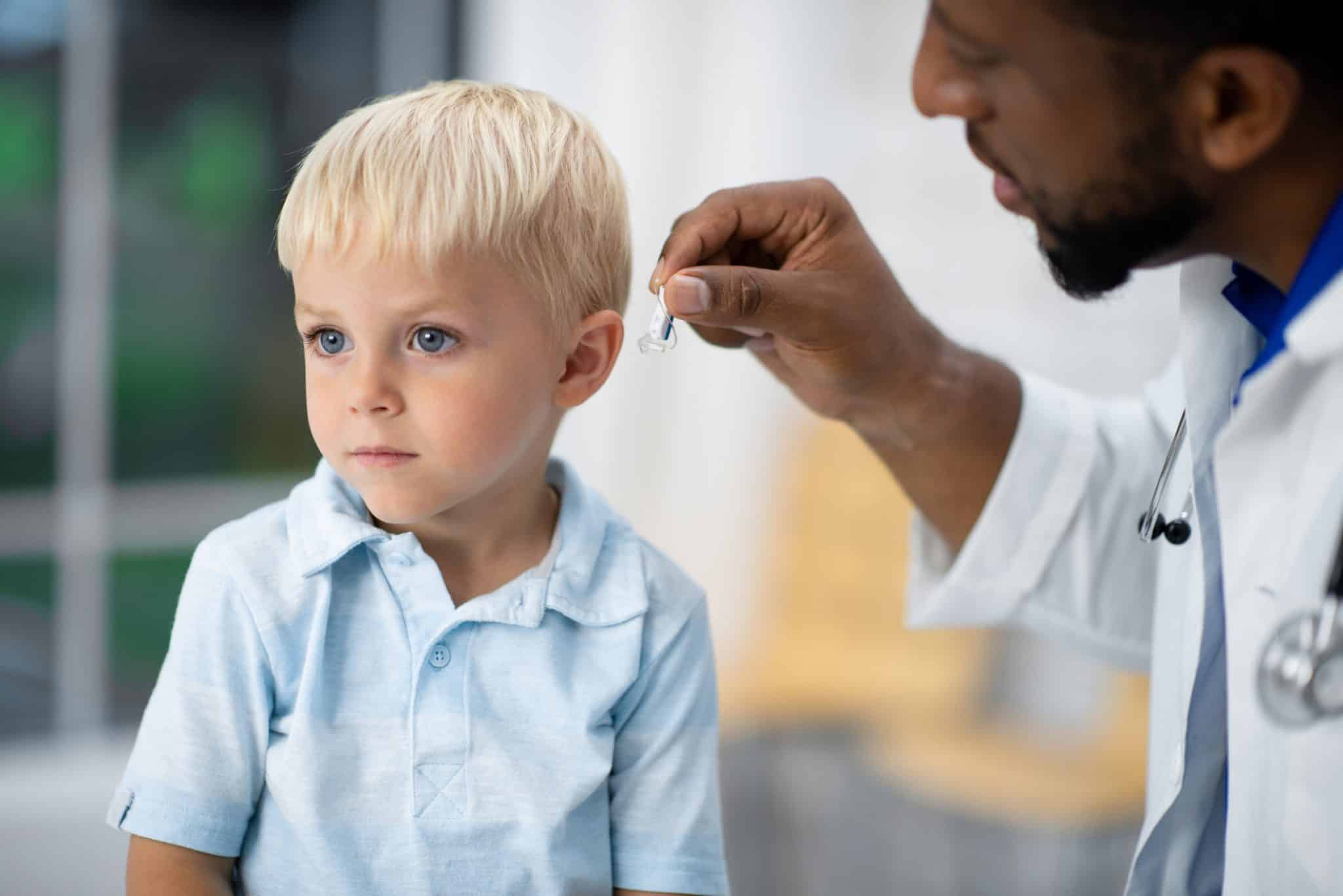 An audiologist fits a hearing aid on to a little boy.