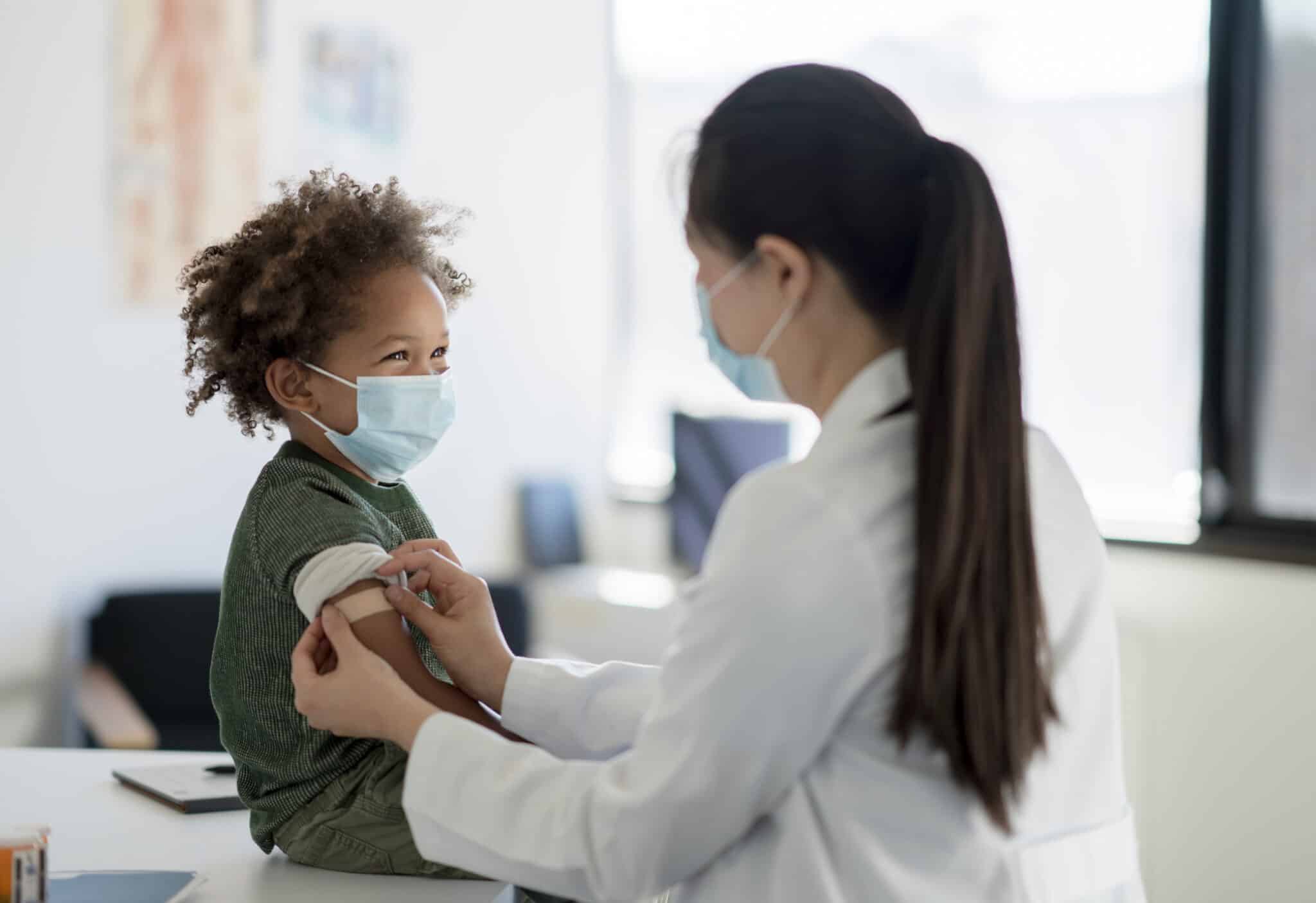 A doctor puts a bandage on a little boy's arm.