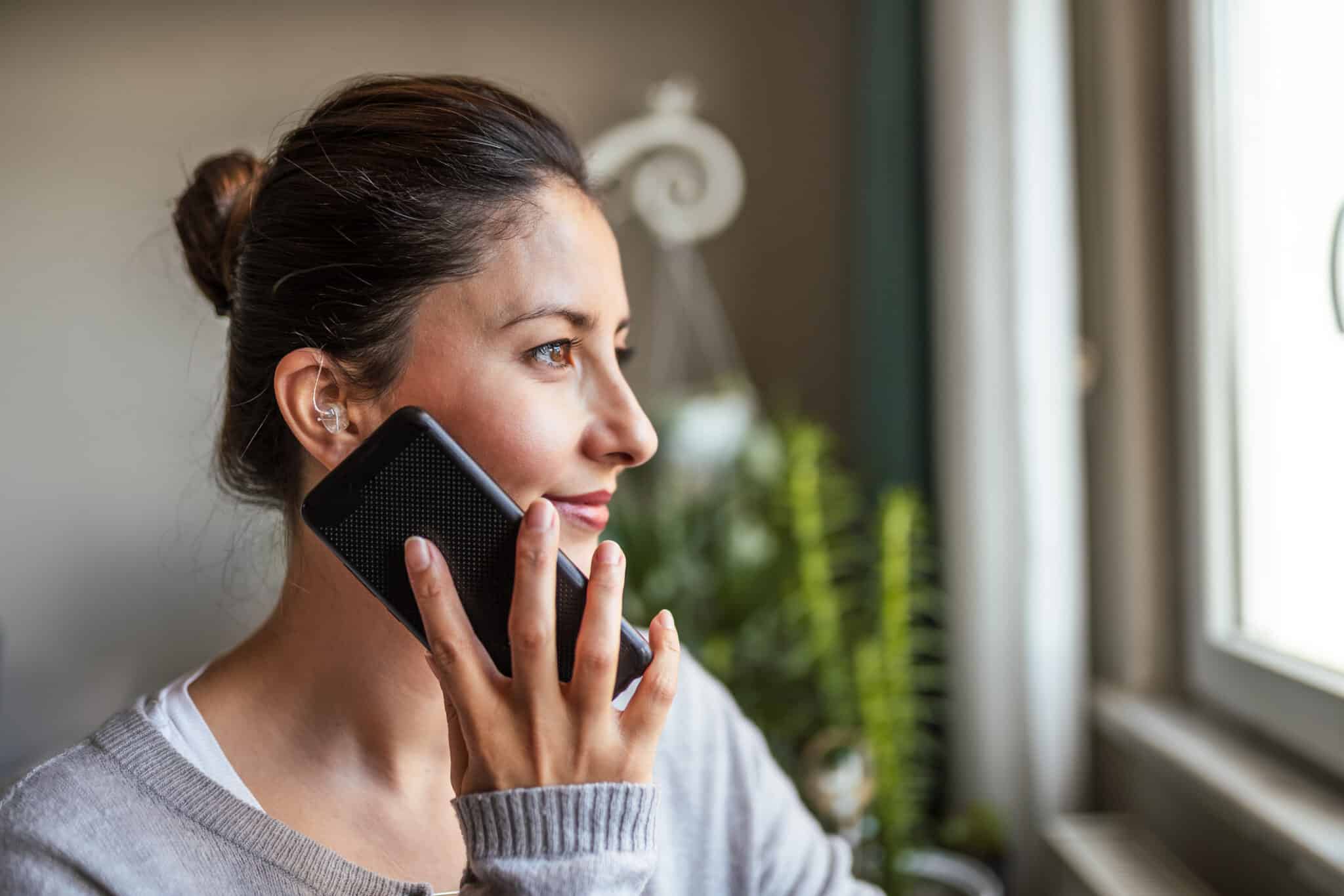Young Adult Woman wearing hearing aids on phone.