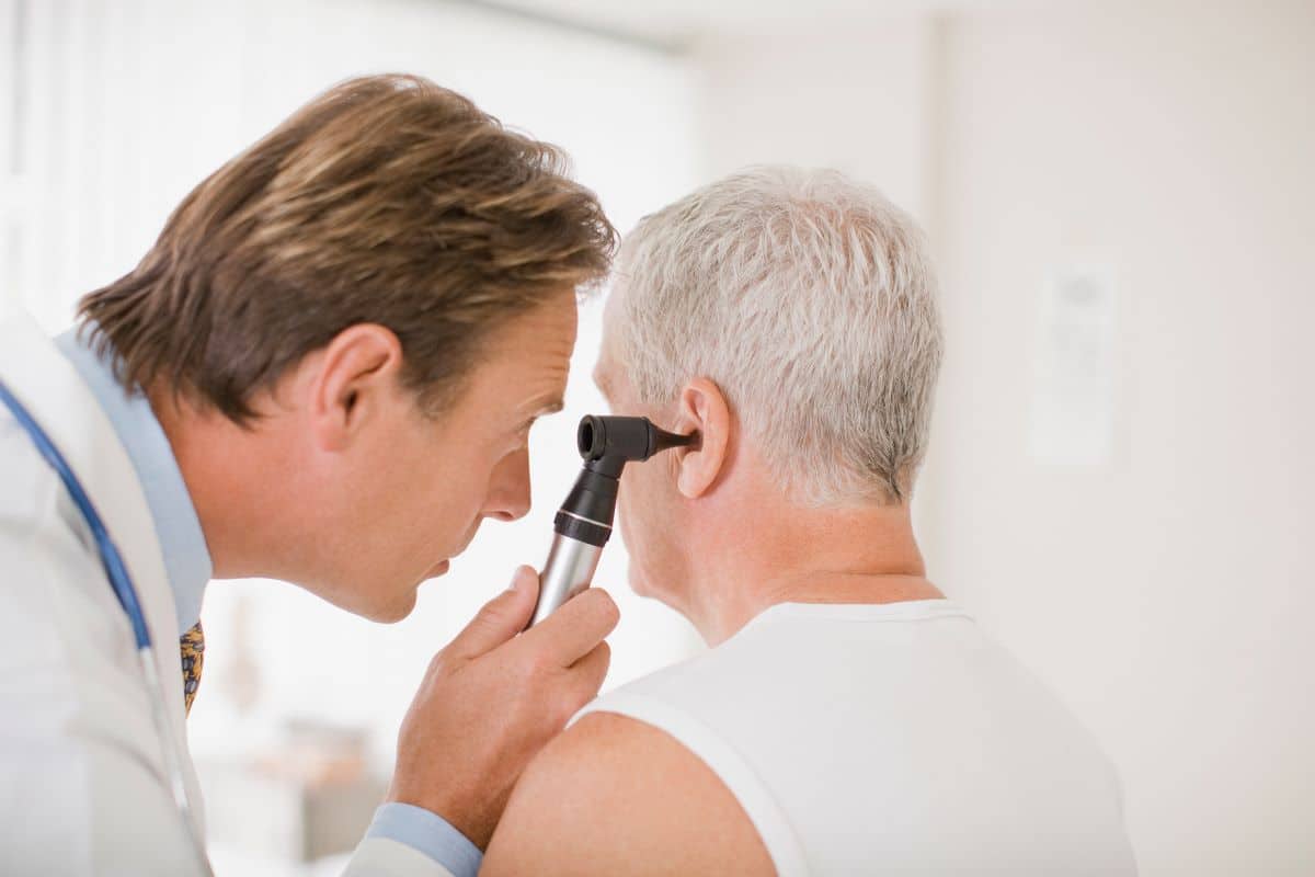 ENT diagnosing acoustic neuroma male doctor looking into older male patients ear using an otoscope