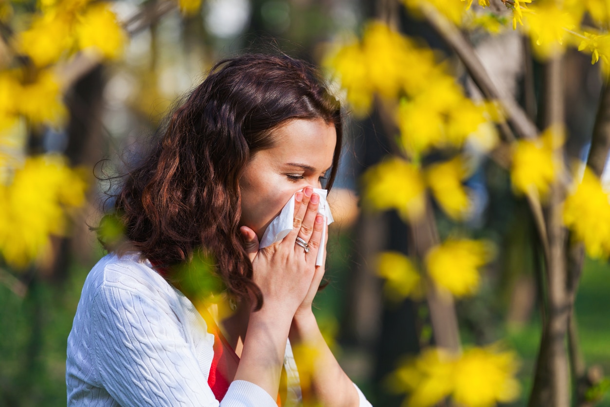 Woman with allergies blowing her nose into a tissue surrounded by flowers