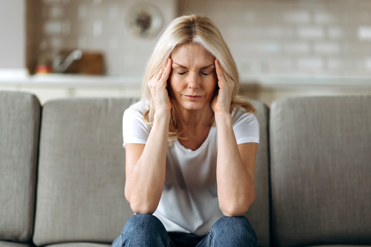 Woman with a headache sitting on her couch rubbing her temples