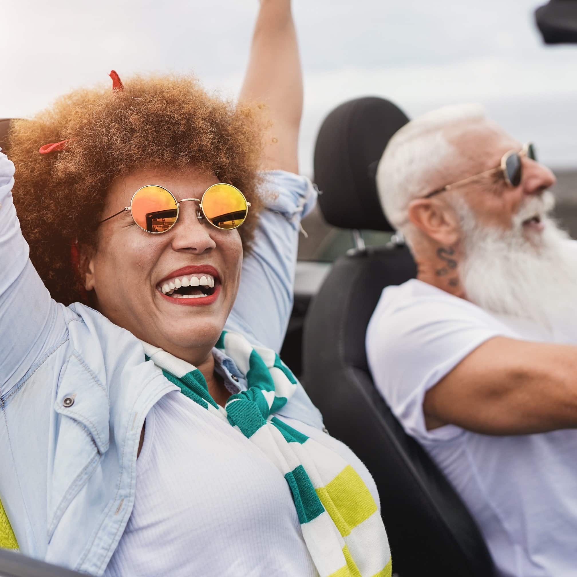 Happy man and woman in a car with the top down.