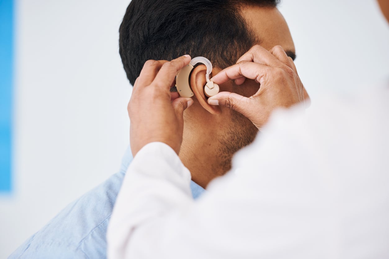 Audiologist putting a hearing aid in the patient's ear during a hearing aid examination appointment.